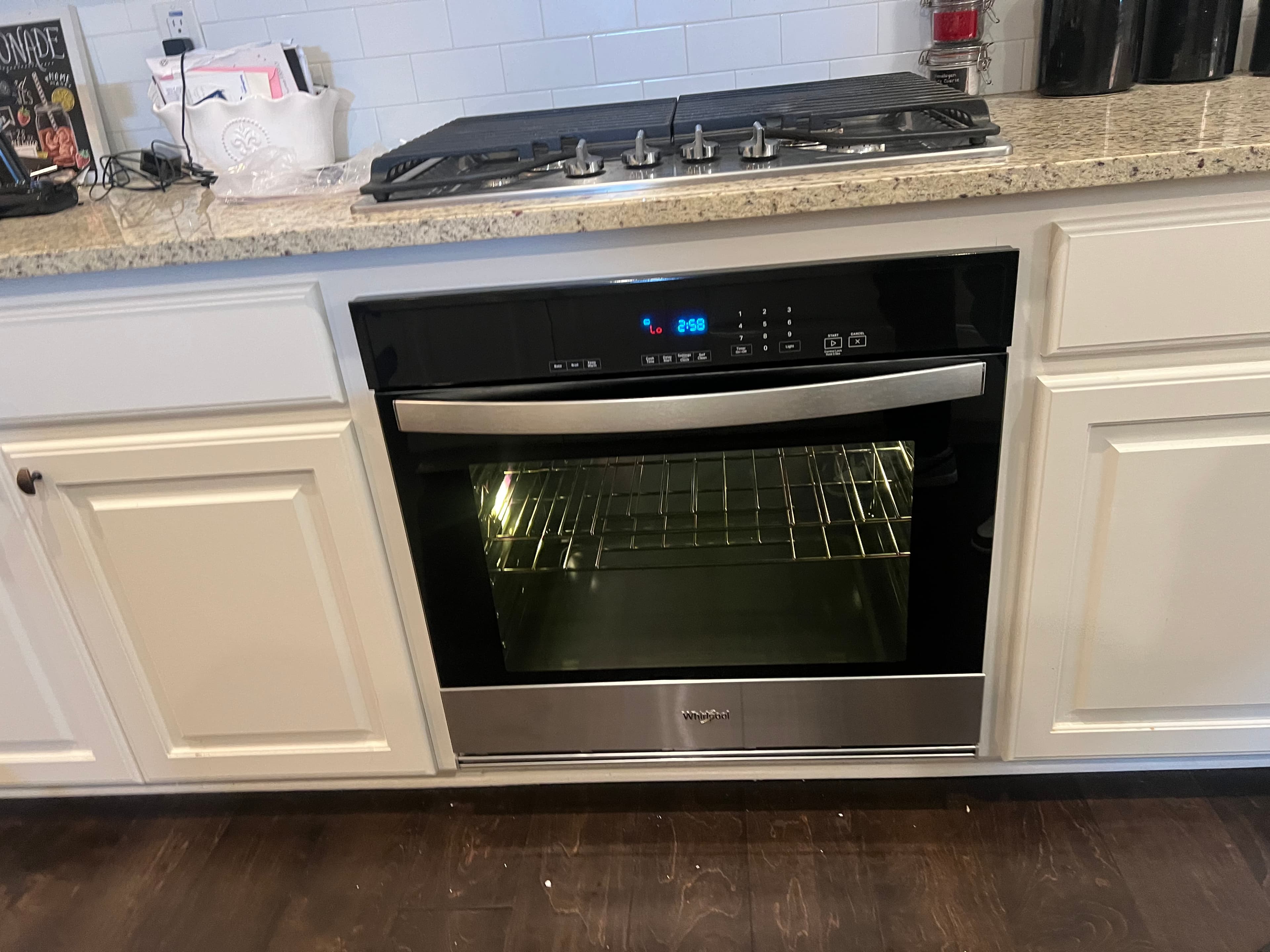 Modern Whirlpool oven built into white kitchen cabinets below a gas stovetop and granite countertop.