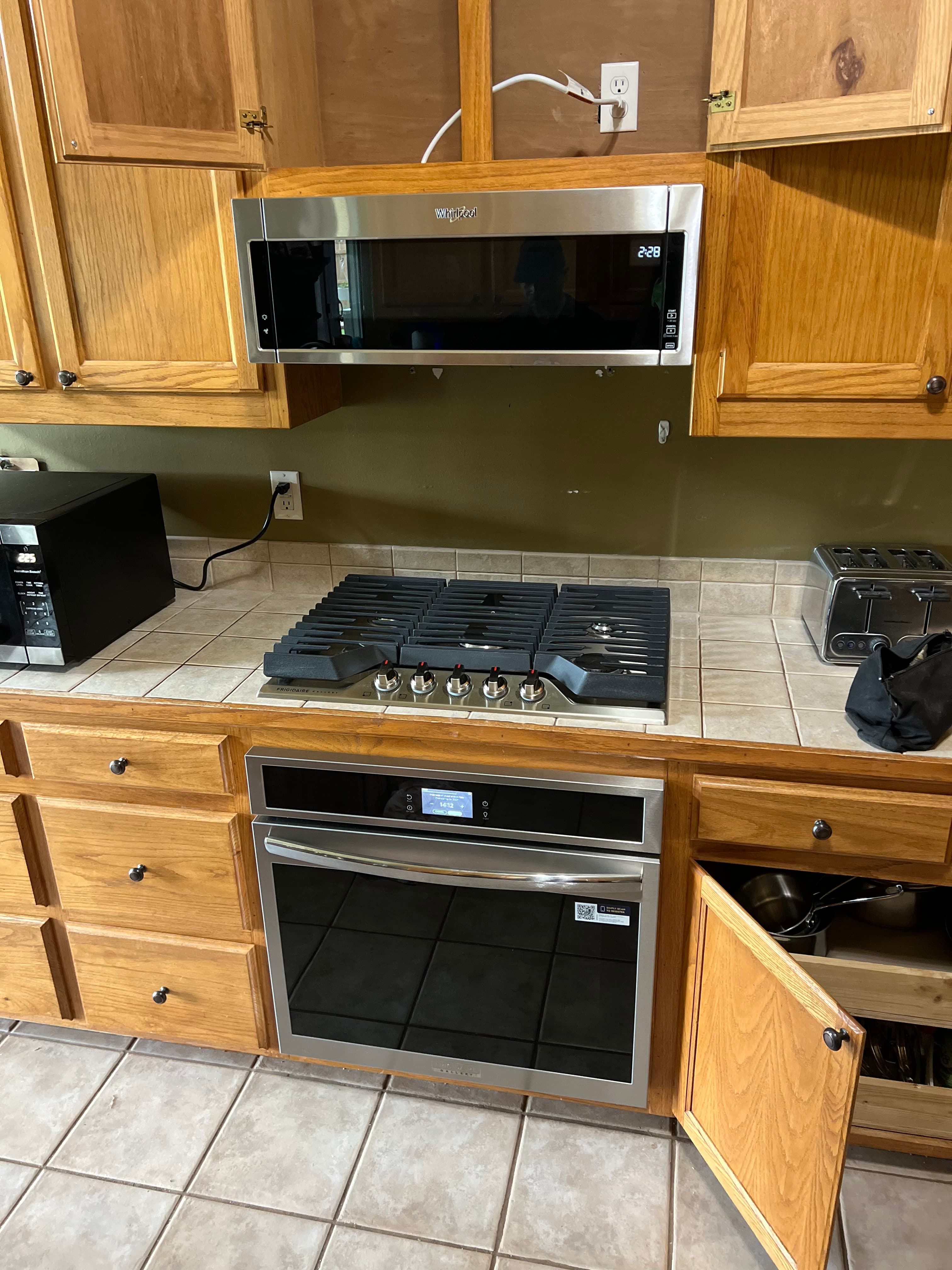 Stainless steel microwave, gas cooktop, and oven built into light wood cabinets with tiled backsplash.