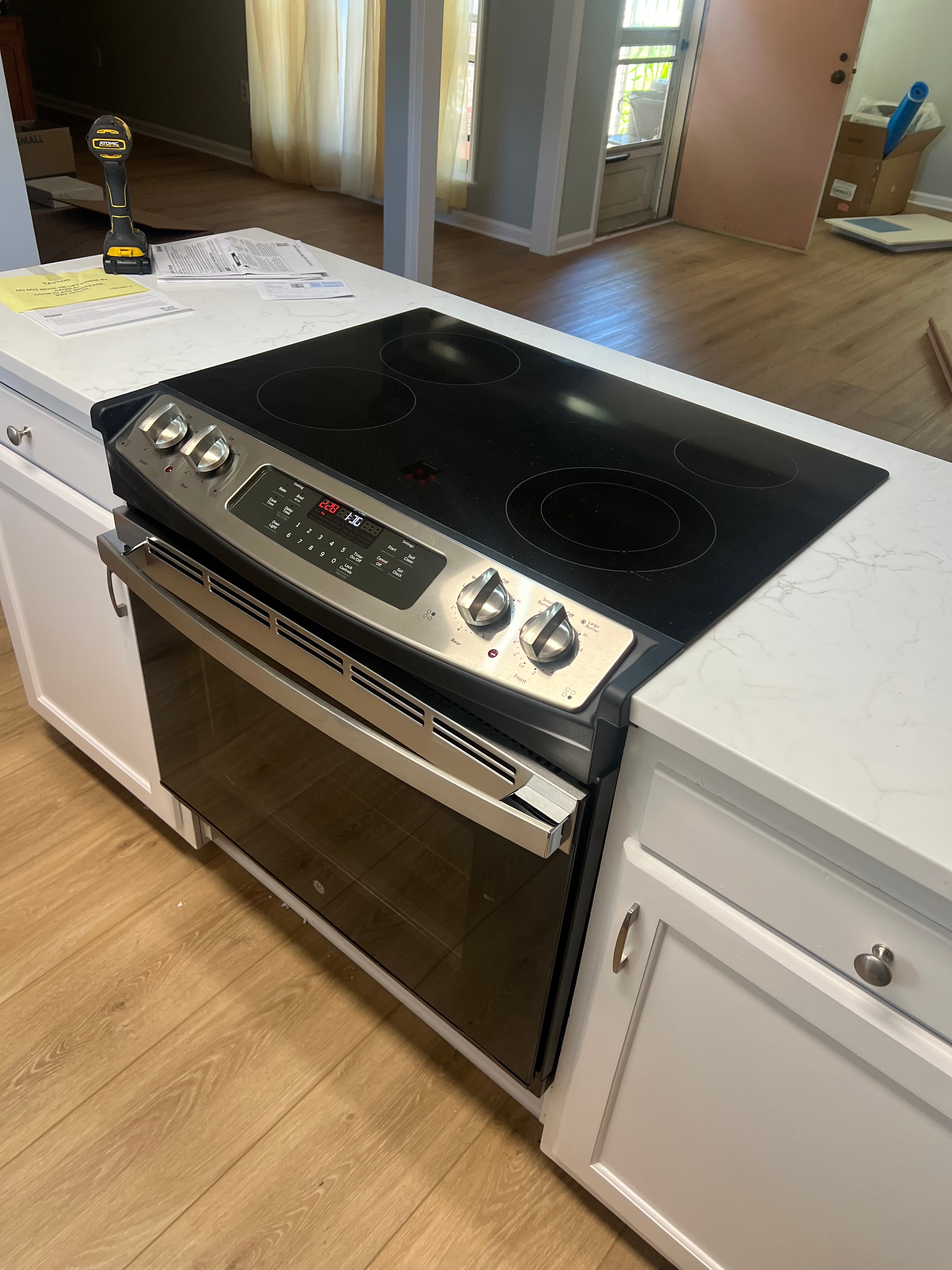Black glass-top electric range with stainless steel controls installed in a white marble kitchen island.