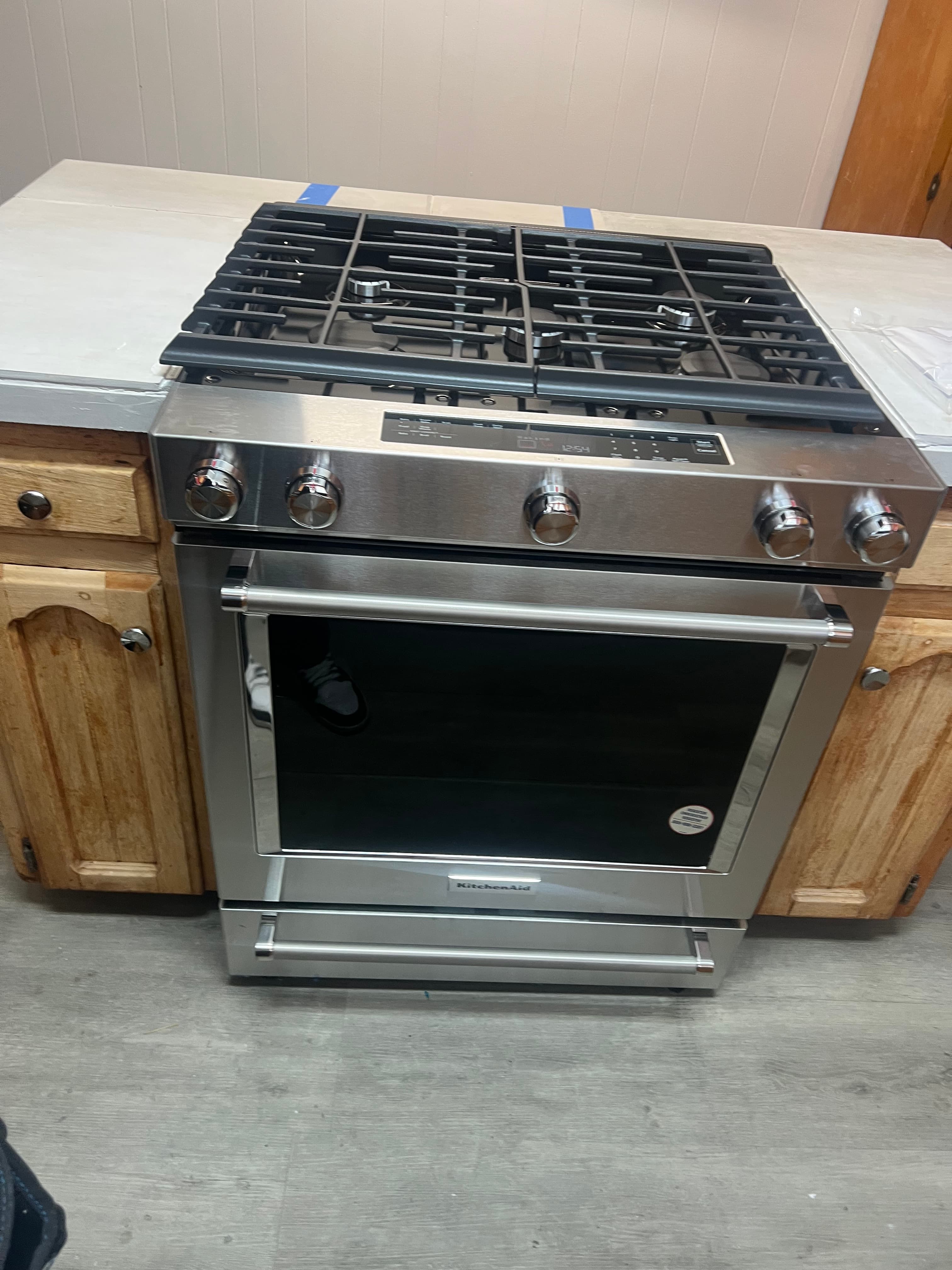 Stainless steel KitchenAid gas range featuring five control knobs and a black glass oven door.