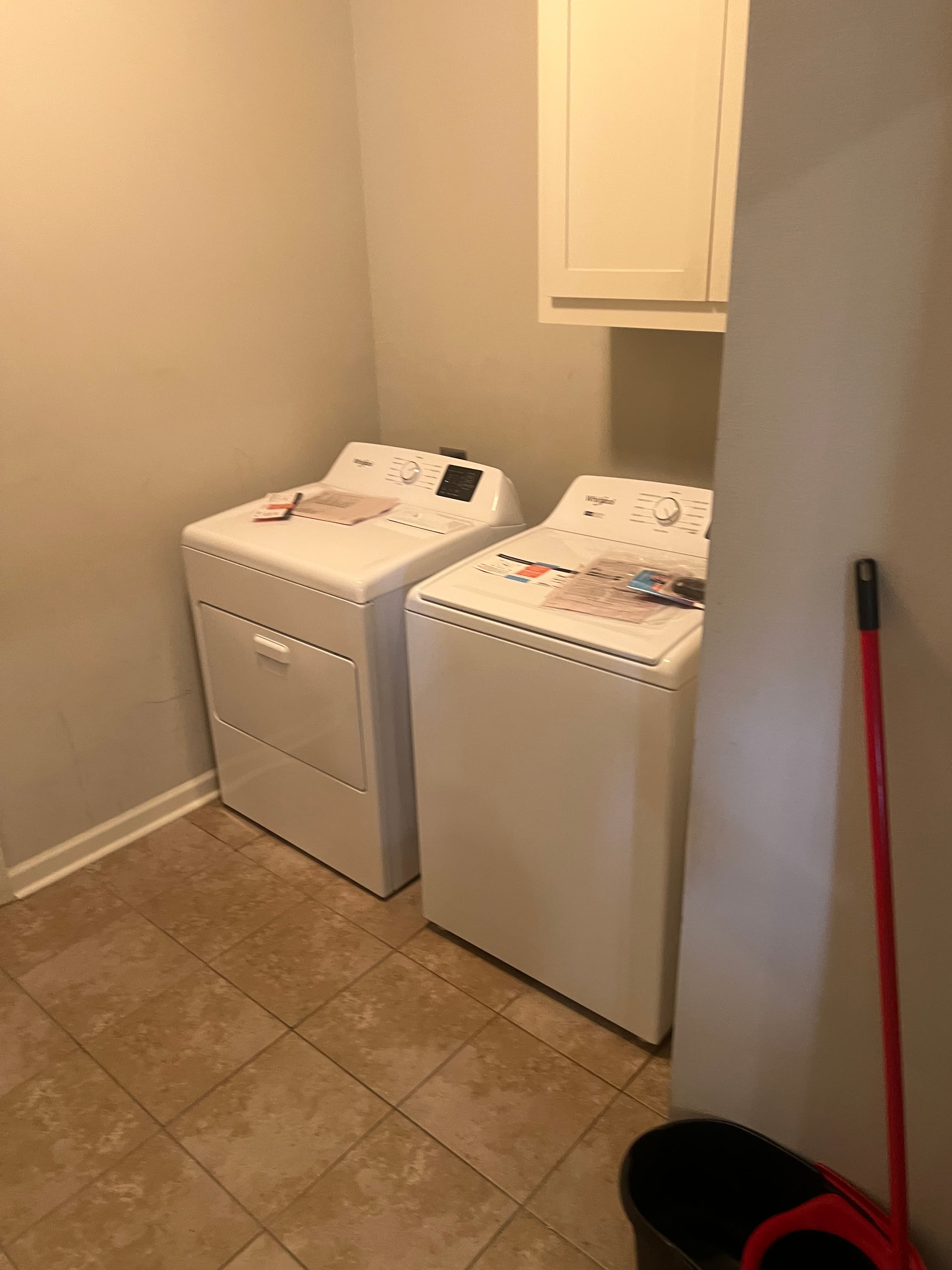 White washing machine and dryer on a beige tiled floor in a laundry room.